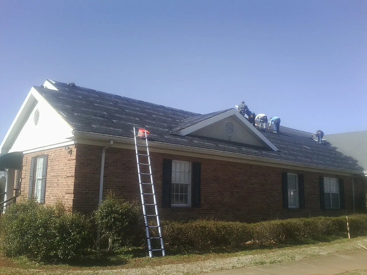 Crew tearing shingles off a brick ranch roof with a ladder set — Emergency Roof Repair work by our crew in Eastford