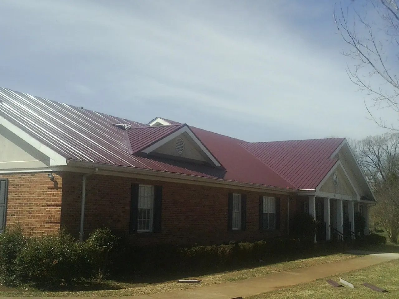 Red metal roof with gabled entries on a long brick building, from a Hail Damage Roof Repair job in Eastford