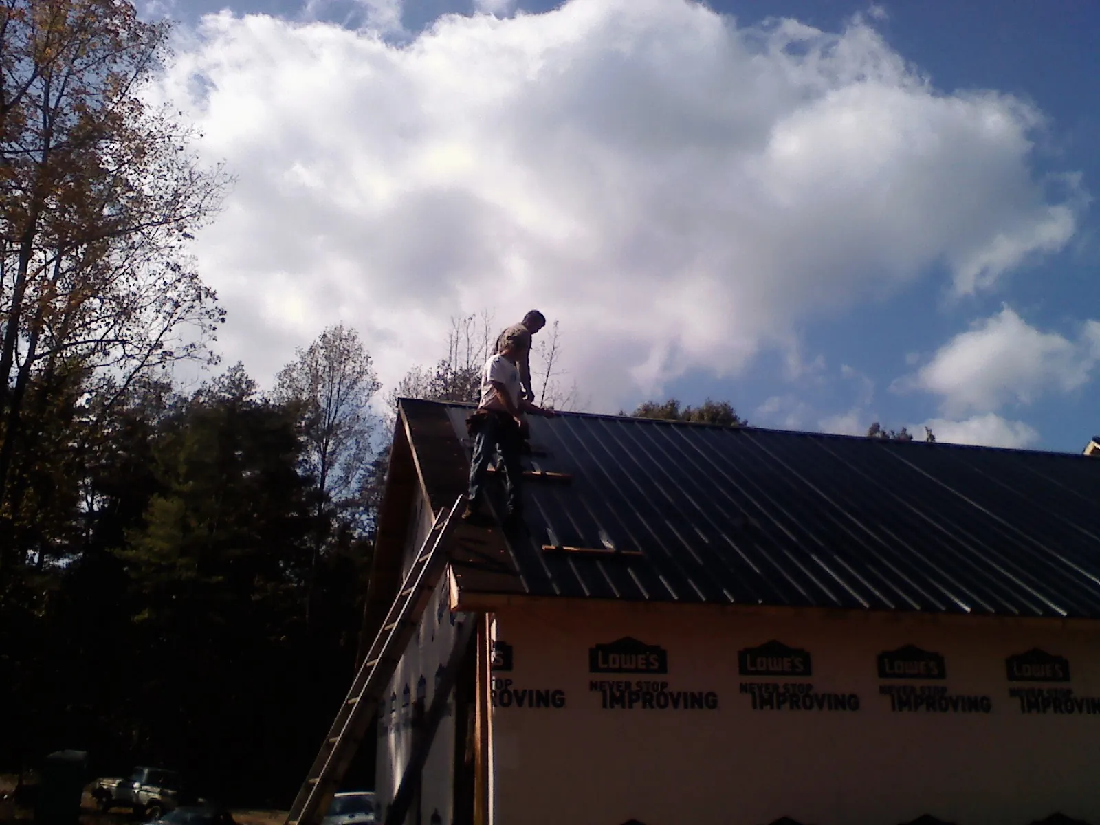 Roofer fastening dark metal panels high against a cloudy sky, from a Roof Inspection job in Eastford