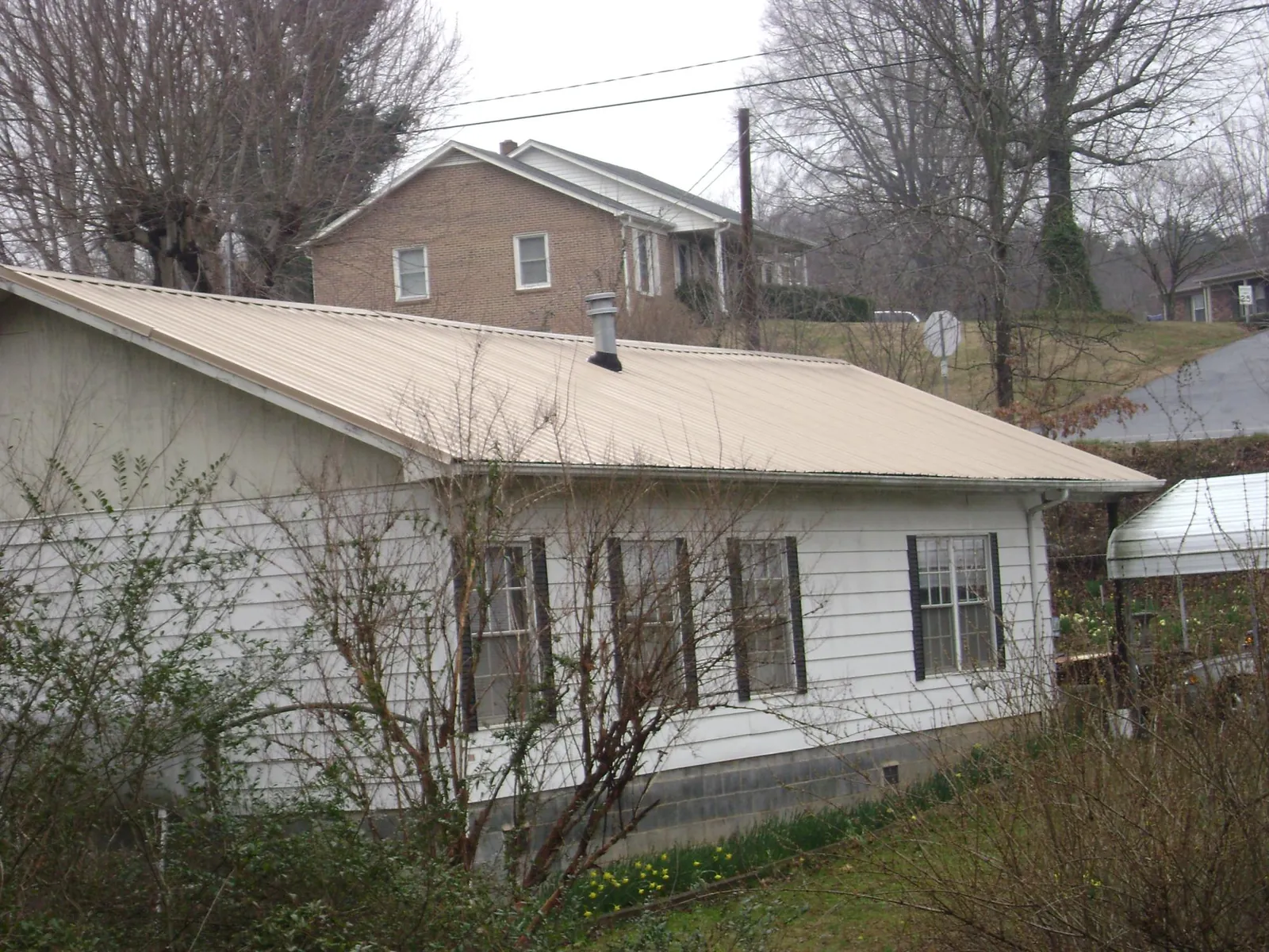 Tan metal roof on a white sided house set into a hillside — Commercial Roofing by Roofing Brothers in Eastford