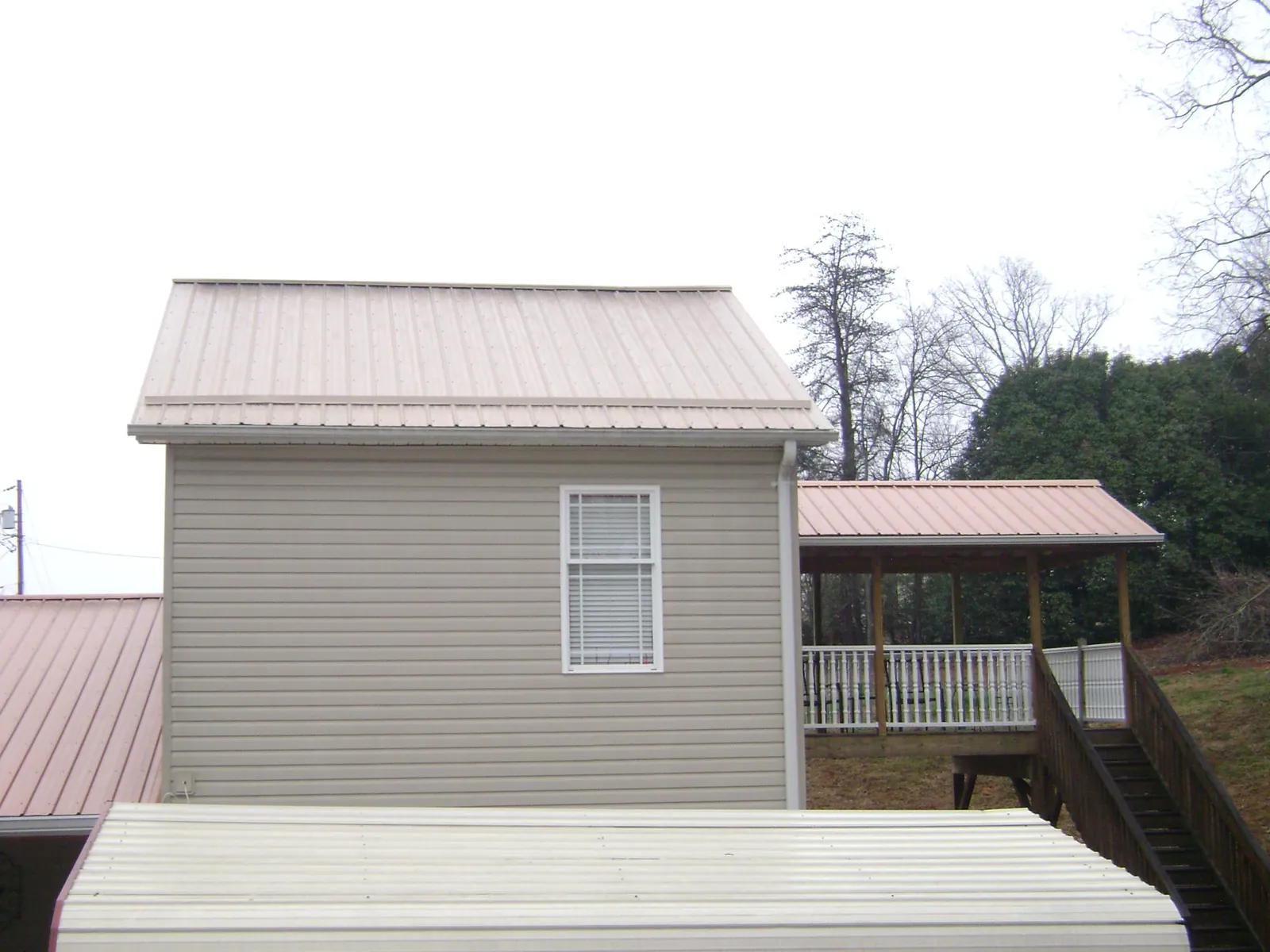 Tan metal roofs on a two story addition and attached porch, from a Roof Replacement job in Eastford